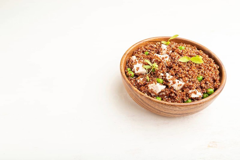 Quinoa porridge with green pea and chicken in wooden bowl on a white wooden background. Side view, close up, copy space