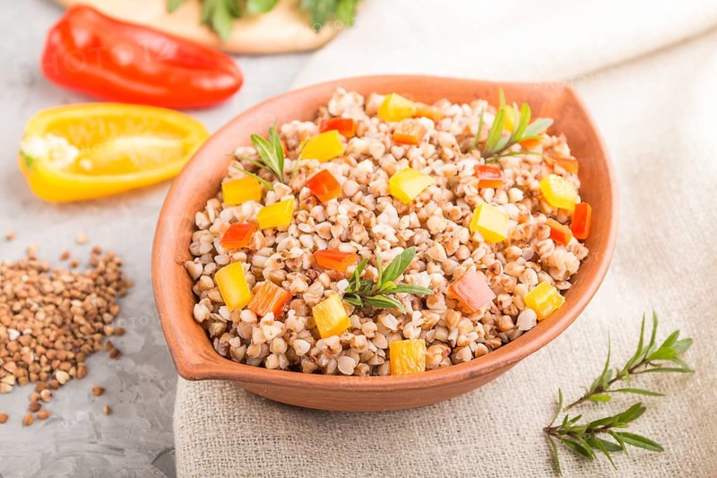 Buckwheat porridge with vegetables in clay bowl on a gray concrete background and linen textile. Side view, selective focus, close up. Russian traditional cuisine