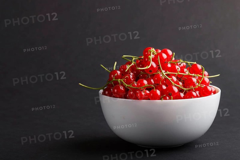 Fresh red currant in white bowl on black background. side view, copy space, close up