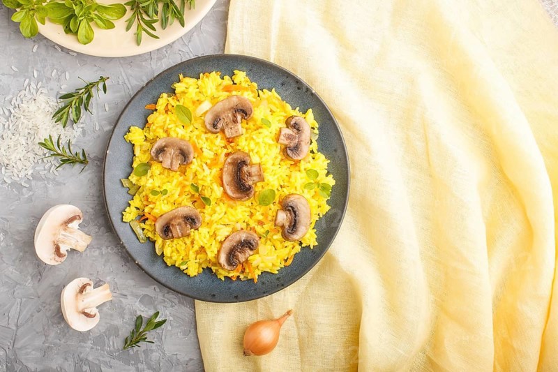 Yellow fried rice with champignons mushrooms, turmeric and oregano on blue ceramic plate on a gray concrete background and yellow textile. Top view, flat lay, copy space