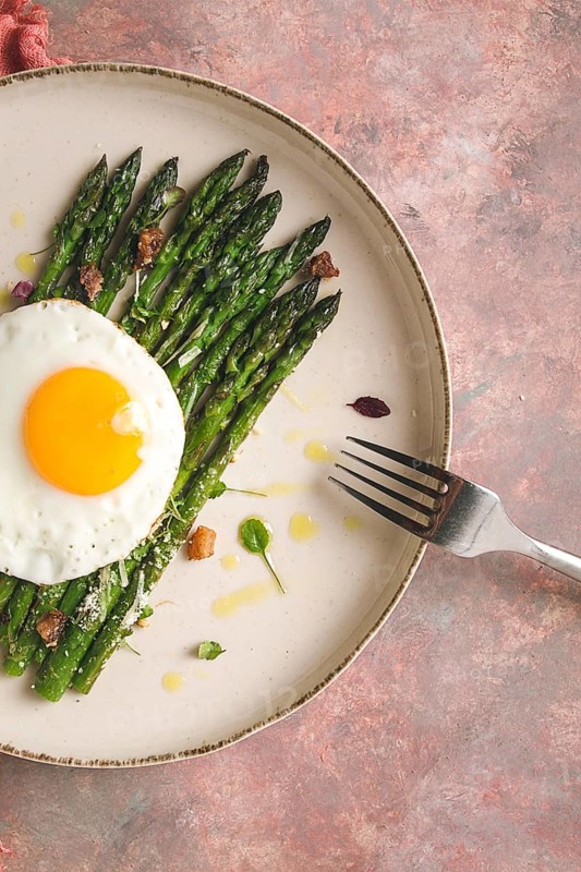Grilled asparagus, with fried egg, spices and herbs, parmesan cheese, on a beige plate, top view, rustic, no people
