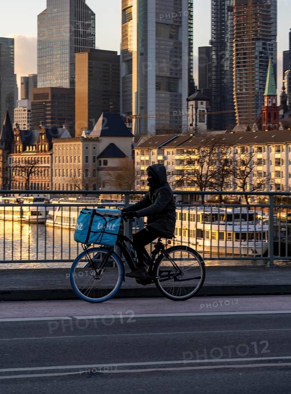 Skyline of the city centre of Frankfurt am Main, cyclist on the Alte Brücke, Wolt delivery service, dusk, river Main, winter, Hesse, Germany, Europe