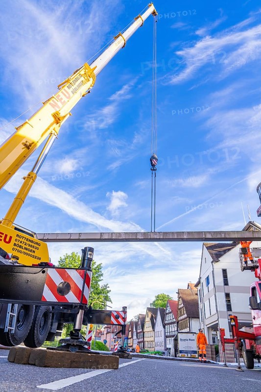 A yellow lifting crane on a busy construction site under a blue sky with buildings in the background, Hermann Hesse railway construction site, Calw, Black Forest, Germany, Europe