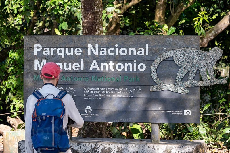 Tourist standing in front of sign at the entrance of the national park, Manuel Antonio National Park, Puntarenas district, Costa Rica, Central America