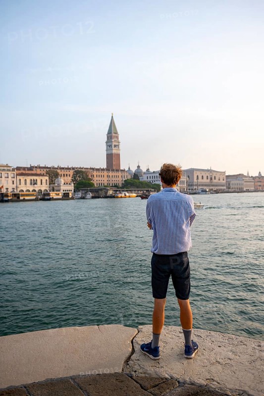 Young man in striped shirt and shorts on the banks of the Grand Canal, behind Campanile, Venice, Veneto, Italy, Europe