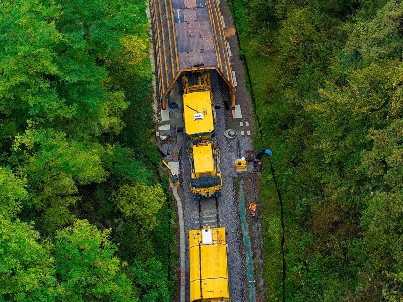 Yellow train exits a tunnel surrounded by forest while workers stand on the tracks, tamping machine, Hermann Hessebahn, Althengstett, Black Forest, Germany, Europe