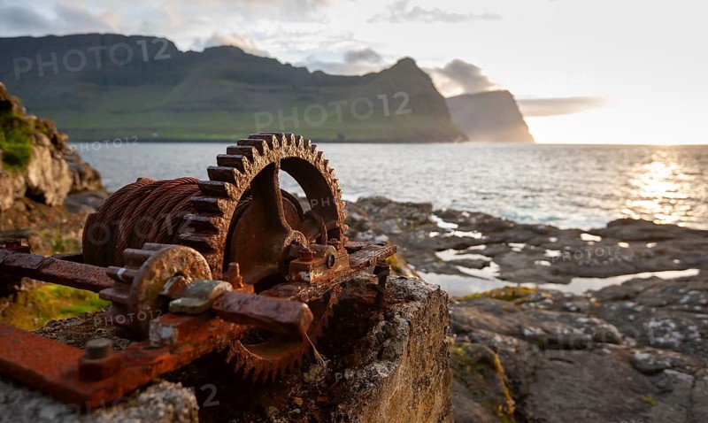 Iron winch with large cogwheel, designed to pull boats ashore, sea with mountains and low sun, Vidareidi, Vidoy Island, Viðareiði, Viðoy Island, Faroe Islands, Denmark, Europe