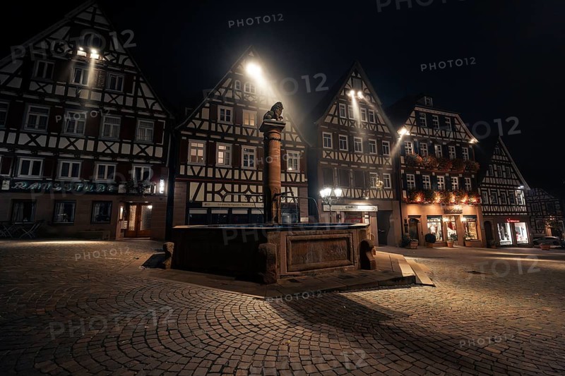 Illuminated square with fountain and half-timbered houses at night, cobblestones emphasise the historic atmosphere, Calw, Black Forest, Germany, Europe