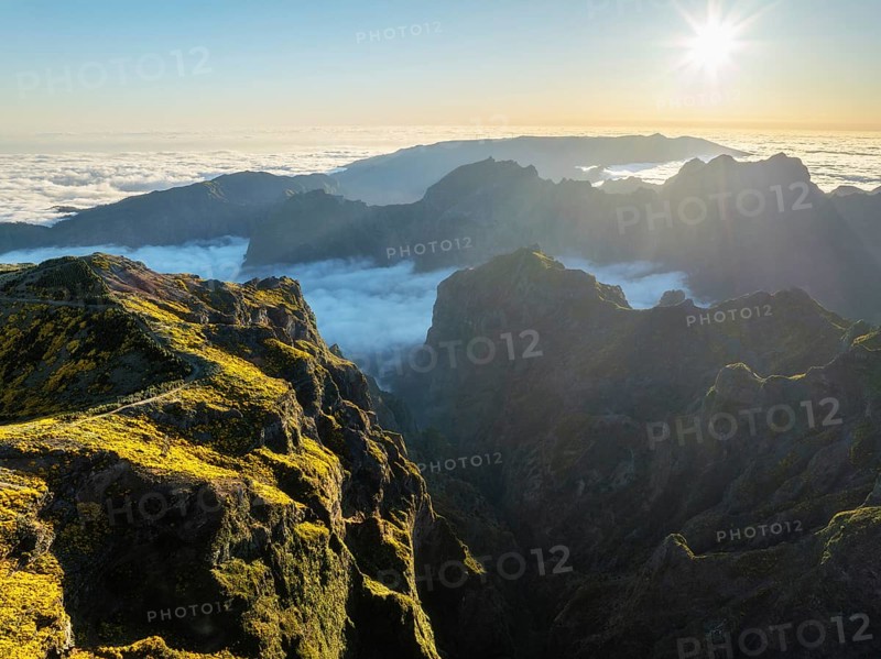 Aerial view at Pico do Arieiro of mountains over clouds with blooming Cytisus shrubs on sunset with sunburst. Madeira island, Portugal, Europe