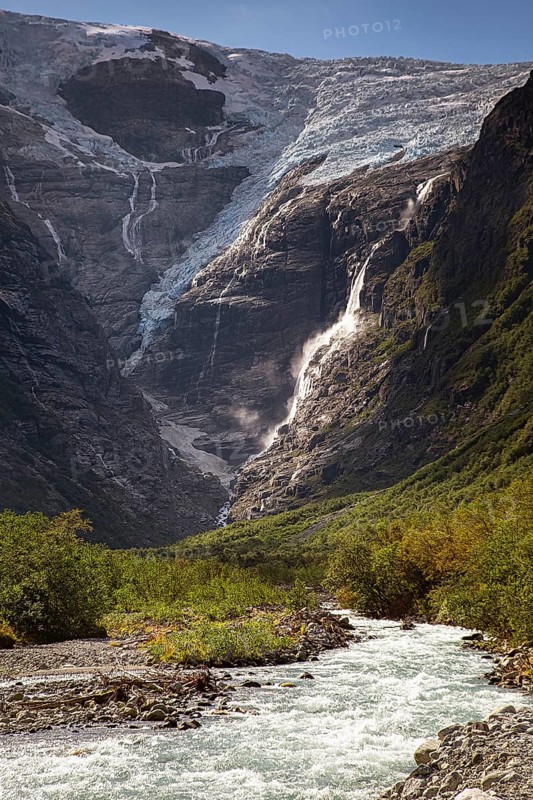 The melting glacier Kjenndalsbreen feeds a waterfall that flows into a wild river, surrounded by mountains in the municipality of Stryn in Vestland, Norway Europe
