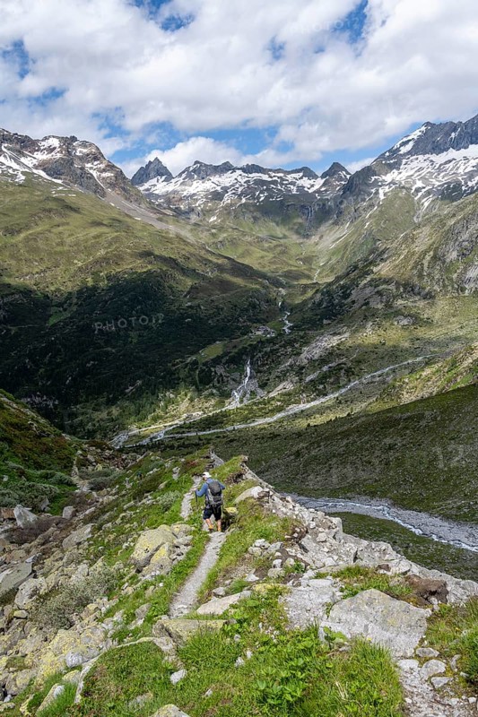 Mountaineer on hiking trail in front of picturesque mountain landscape, rocky mountain peaks with snow, valley Zemmgrund with Zemmbach, mountain panorama with summit Großer Mörchner and Zsigmondyspitze, Berliner Höhenweg, Zillertal Alps, Tyrol, Austria, Europe
