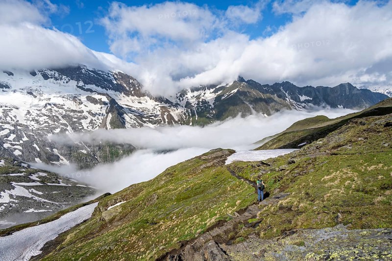 Mountaineer on hiking trail, mountain panorama with high fog in the valley, summit Hochfeiler, Hoher Weißzint and Hochsteller with glacier Schlegeiskees, Berliner Höhenweg, Zillertal Alps, Tyrol, Austria, Europe