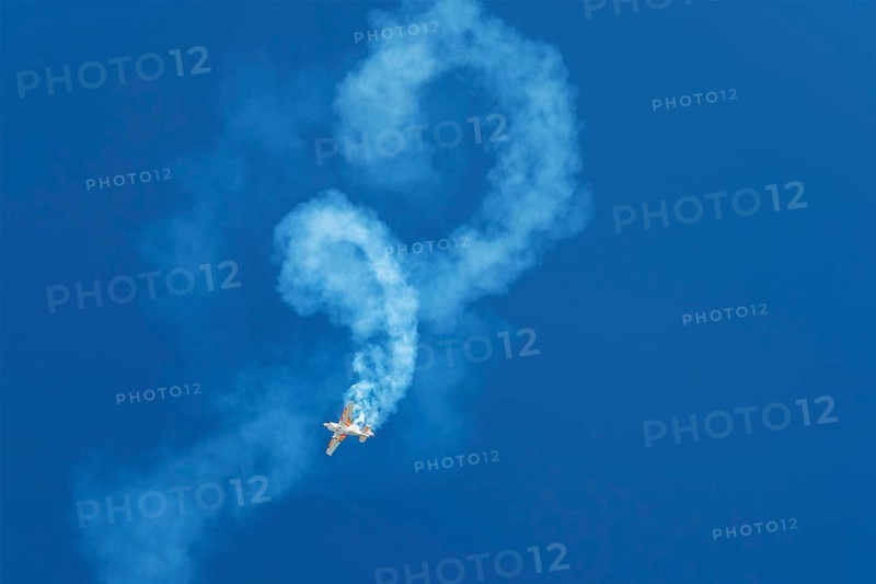 Stunt aerobatic plane performing stunts rolls loops in blue sky with smoke trail. Concept of speed, difficulty, precision, risk, challenge
