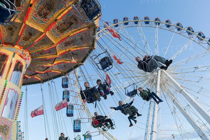 People swinging on a carousel in front of a Ferris wheel in sunny weather at a funfair, Europa Rad, Cannstadter Volksfest, Stuttgart-Bad Cannstadt, Baden-Württemberg