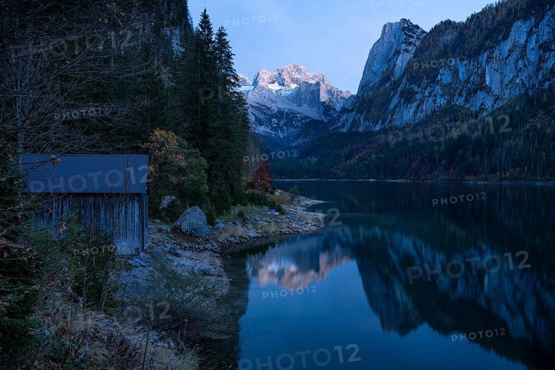 The Vordere Gosausee lake in autumn with a view of the Dachstein mountain range. The Gosaukamm on the right. Good weather, blue sky. In the evening, after sunset. Reflection. A small wooden hut on the left. Vorderer Gosausee, Gosau, Gosau valley, Salzkammergut, Upper Austria, Austria, Europe