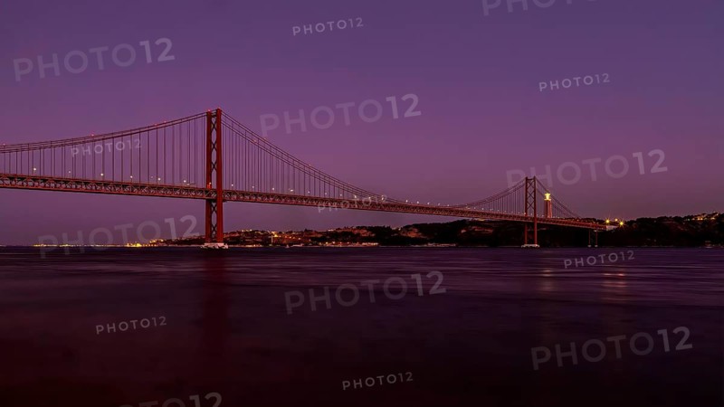 Twilight descends on a calm river with a suspension bridge standing majestically against a purple sky, Lissabon, 25 de Abril Bridge