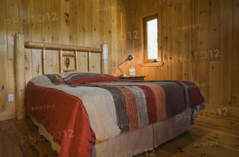 Queen size bed covered with colorful striped bedspread and rustic white pine log headboard in master bedroom inside Scandinavian log cabin home, Quebec, Canada, North America