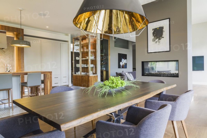 Chrome and walnut wood table with charcoal linen armchairs and large black and gold industrial style pendant lighting fixture in dining room area inside a luxurious contemporary bungalow style home, Quebec, Canada, North America