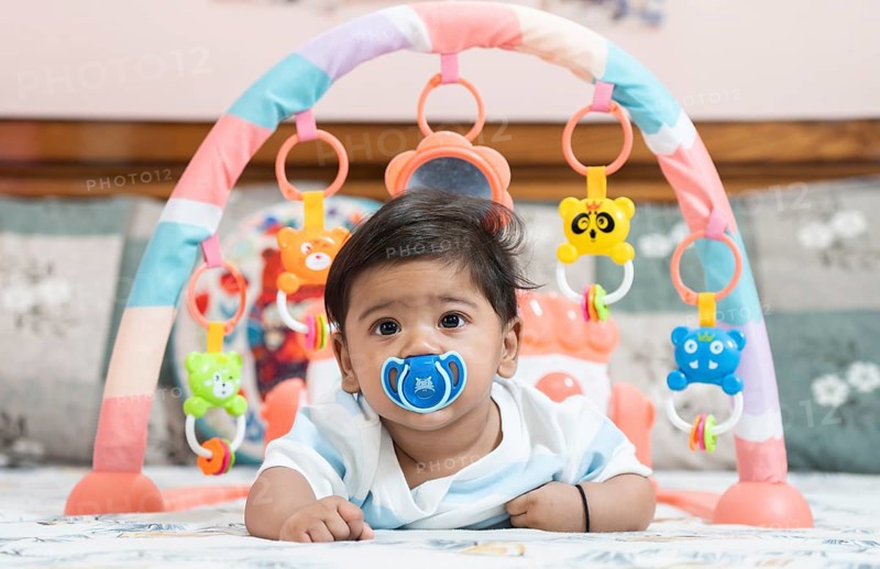 Baby boy playing lying on bed with pacifier on mouth