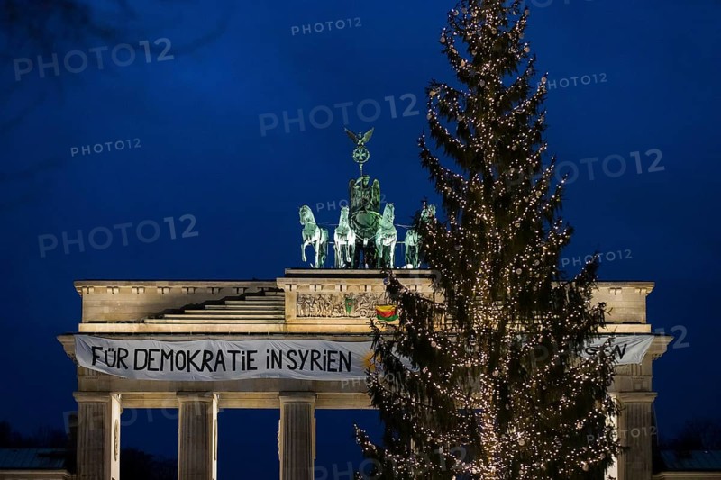 A banner For Democracy in Syria / Defend Rojava hangs behind a Christmas tree at the Brandenburg Tor, Berlin, 16 December 2024