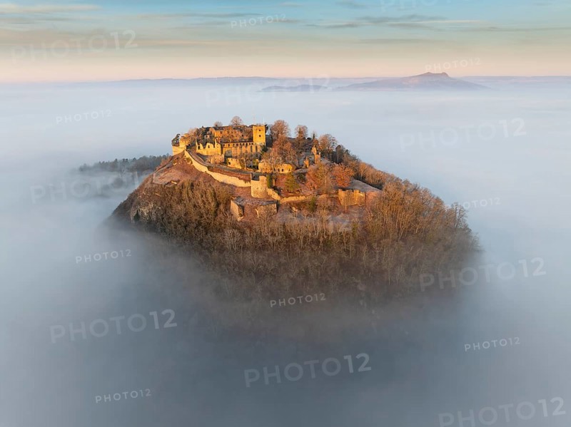 Aerial view of the Hegau volcano Hohentwiel with the upper fortress ruins illuminated by the rising sun, which rises out of the fog during an inversion weather situation, on the horizon the Hohenstoffeln, district of Constance, Baden-Württemberg, Germany, Europe