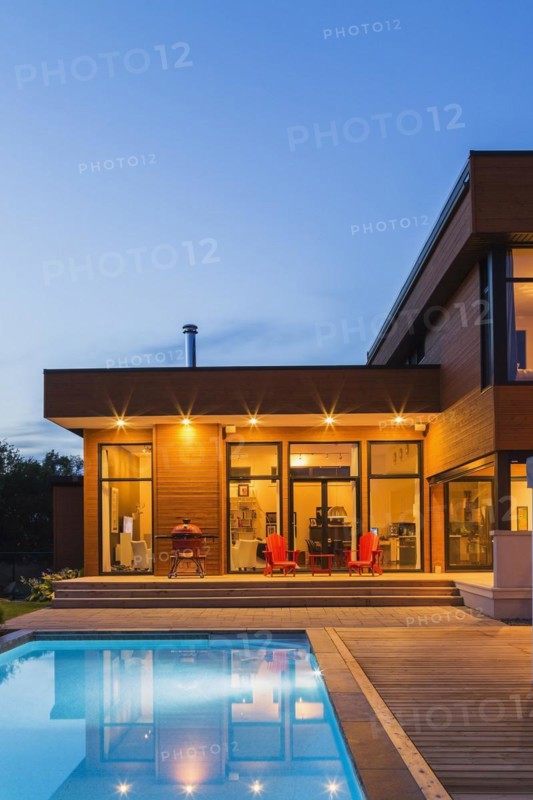 Modern cube style home with stained horizontal wood cladding and in-ground swimming pool at dusk, Quebec, Canada, North America