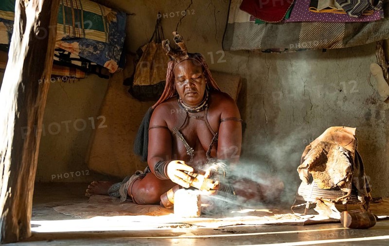Traditional Himba woman prepares herbs for body care with smoke, Interior of the first woman's mud hut in a Himba village, Traditional containers for ochre colour and woven frame with leather for body care with smoke at Opuwo, Kaokoveld, Kunene, Namibia, Africa