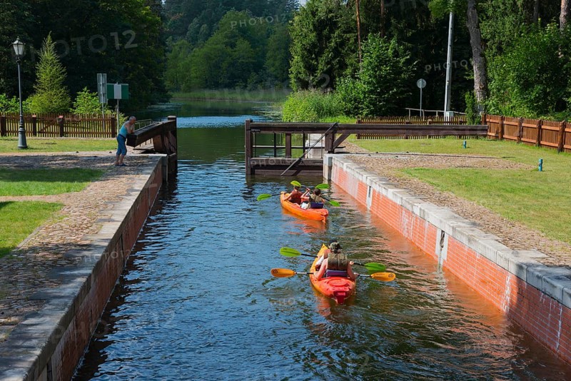 Two canoeists on a water canal under a small bridge in a wooded area, Sluza Perkuc, Perkuc lock, Kanal Augustowski, Augustów Canal, Augustow, canal, Plaska, Plaska, Powiat Augustowski, Podlaskie Voivodeship, Poland, Europe