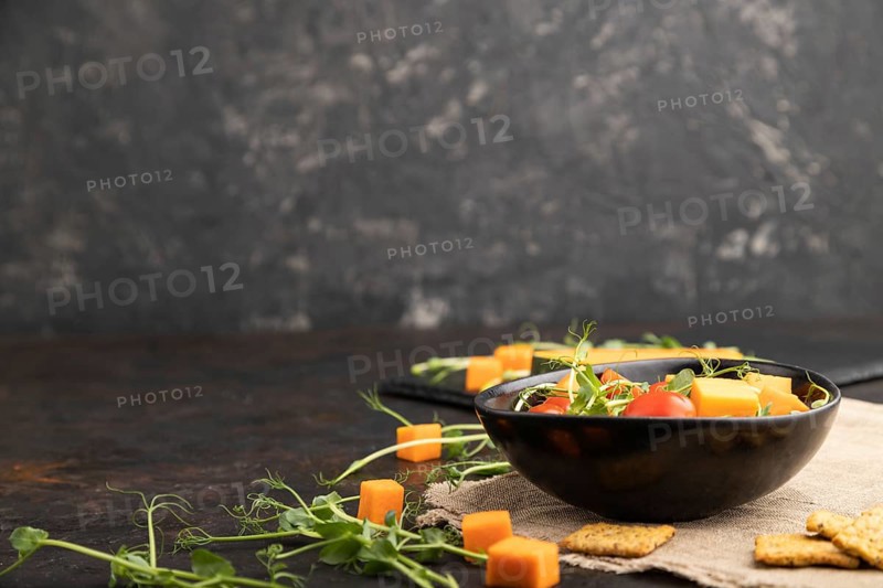 Vegetarian vegetable salad of tomatoes, pumpkin, microgreen pea sprouts on black concrete background and linen textile. Side view, copy space