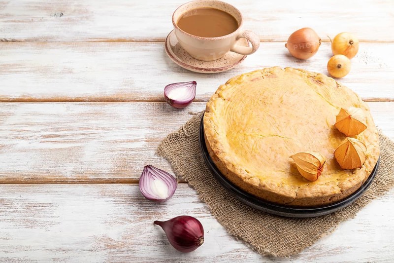 Autumn onion pie and cup of coffee on white wooden background and linen textile. Side view, copy space