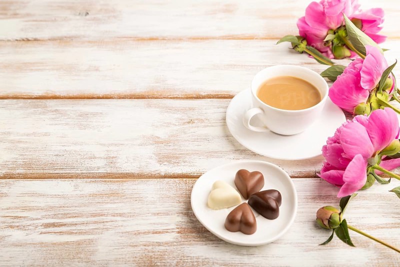 Cup of cioffee with chocolate candies, pink peony flowers on white wooden background. side view, copy space, still life. Breakfast, morning, spring concept
