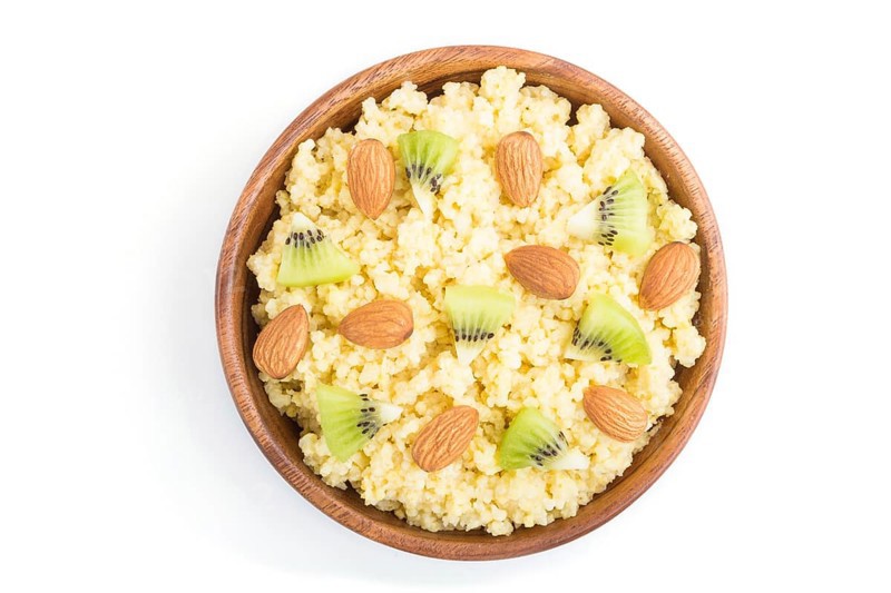 Millet porridge with kiwi and almonds in wooden bowl isolated on white background. Top view, flat lay, close up