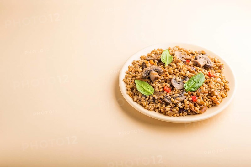 Spelt (dinkel wheat) porridge with vegetables and mushrooms on ceramic plate on orange background. Side view, copy space. Russian traditional cuisine