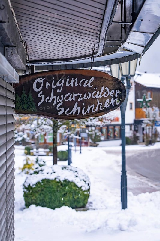 Company sign for Black Forest ham on a snowy street with shops, Enzklösterle, district of Calw, Black Forest, Germany, Europe