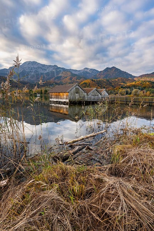 Boathouses in the lake at sunrise, Lake Kochel in autumn with reflection, behind mountain peaks Herzogstand and Heimgarten Upper Bavaria, Bavaria, Germany, Europe