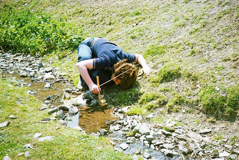 Secondary school student doing geographical fieldwork, Great Britain 1970s: Girl measuring the depth of a small stream with a ruler, 1977