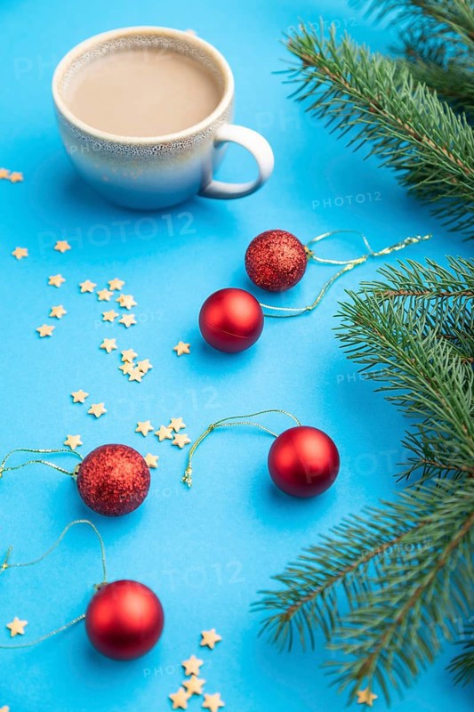 Christmas or New Year composition. Decorations, red balls, fir and spruce branches, cup of coffee, on a blue paper background. Side view, close up