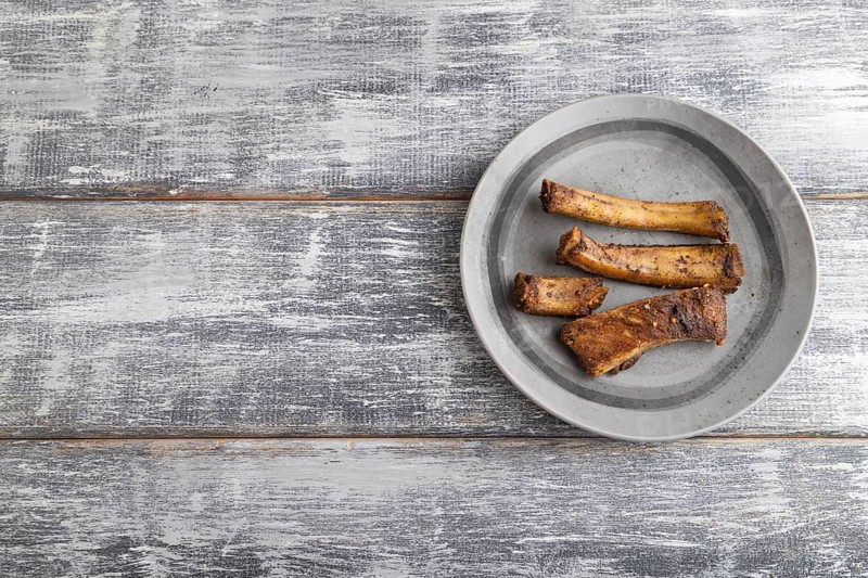 Pork ribs on a wooden plate on a gray wooden background. Top view, flat lay, close up, copy space
