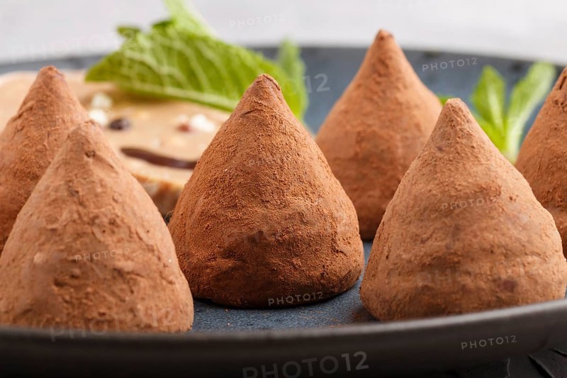 Chocolate truffle on blue ceramic plate on gray concrete background. close up, side view