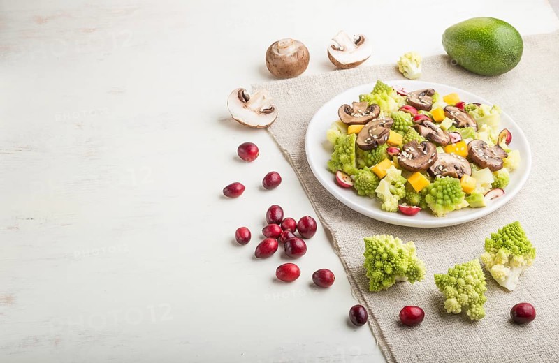 Vegetarian salad from romanesco cabbage, champignons, cranberry, avocado and pumpkin on a white wooden background and linen textile. side view, copy space