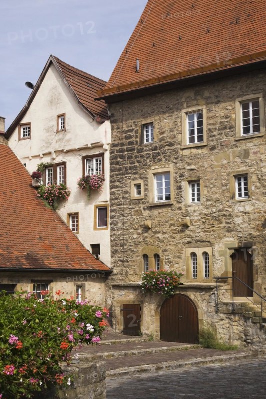 Old stone building facade with traditional terracotta ceramic tiled rooftops and windows decorated with Pelargonium, Geranium flowers in late summer, Bad Wimpfen, Germany, Europe