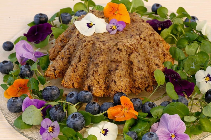 Vegetarian cuisine, chestnut roast, chestnut cake, chestnut roast, chestnut cake with hazelnuts, chestnut cake, savoury, vegan, salty, baked, from the oven, healthy, main course, glass plate, new cuisine, decoration with pansies, violet (Viola), blueberries (Vaccinium), blueberries, food photography, studio, Germany, Europe