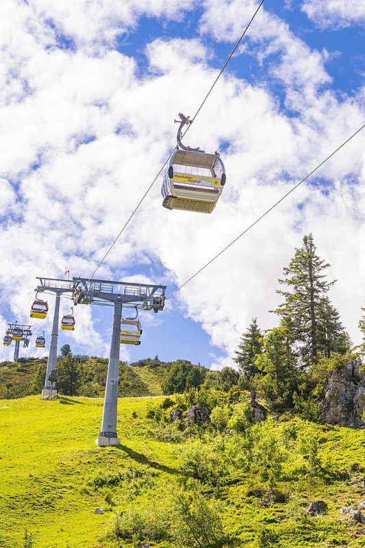 A cable car travelling across a green meadow, surrounded by trees and under a cloudy sky, Penken, Zillertal, Austria, Europe