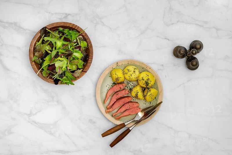 Top view of a rustic meal consisting of fresh green salad, hot smoked humpback salmon and boiled potatoes seasoned with herbs, served on a marble table