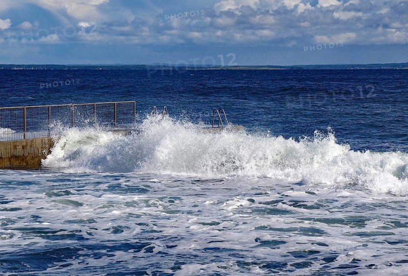 Waves crashing against a railing by the sea under a slightly cloudy blue sky, Tönsberg, Oslofjord, Norway, Europe