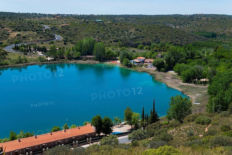 View of a tranquil lake with surrounding houses, trees and hills under a blue sky, view from the viewing platform, Mirador de la Laguna del Rey, Lagunas de Ruidera National Park, Albacete province, Castilla-La Mancha, Spain, Europe