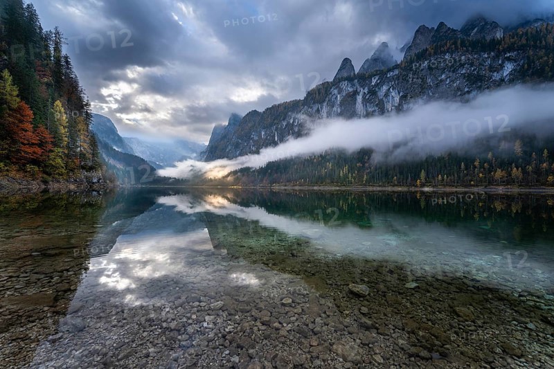 The Vordere Gosausee in autumn with a view of the Gosaukamm on the right. The Dachstein in clouds in the background. Cloudy sky. A spot of sunlight. Reflection. Vorderer Gosausee, Gosau, Gosau valley, Salzkammergut, Upper Austria, Austria, Europe