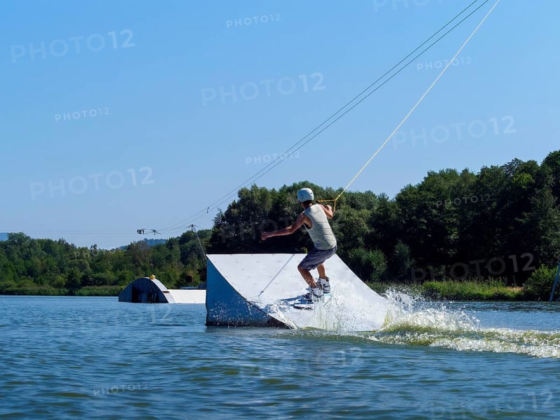 Young man jumping with wakeboard over jump into the lake, water sports, water skiing in wakepark, Stráž pod Ralskem, Czech Republic, Europe