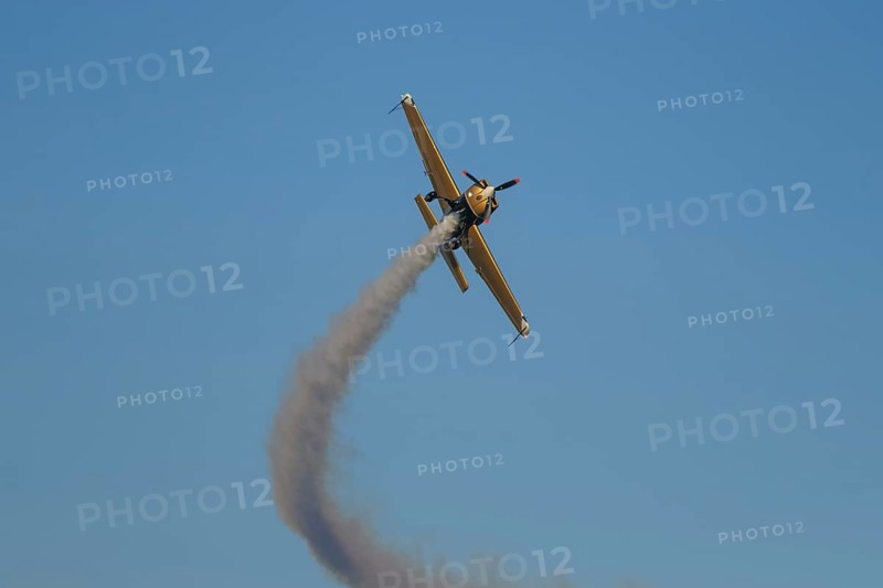 Golden stunt aerobatic plane performing stunts in blue sky with smoke trail. Concept of speed, difficulty, precision, risk