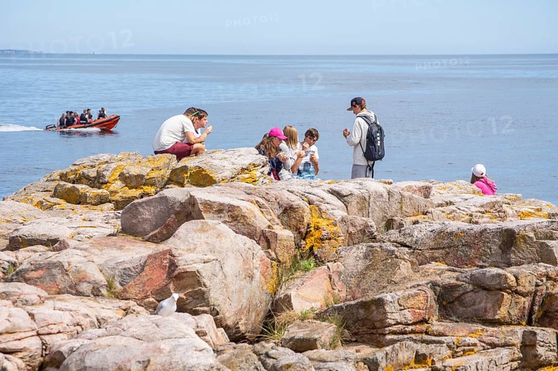People on rocks by the sea with speedboat in the background in Gudhjem, Bornholm, Baltic Sea, Denmark, Scandinavia, Europe